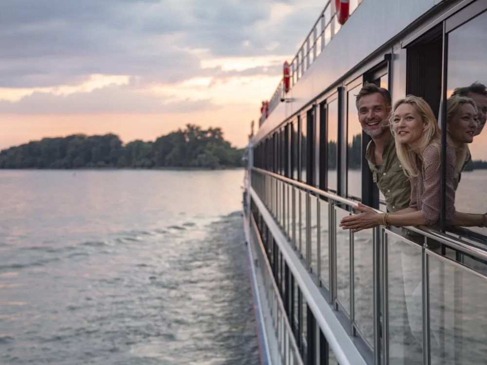 Flusskreuzfahrt mit nicko cruises erleben Paar genießt die Aussicht auf einem Flusskreuzfahrtschiff bei Sonnenuntergang entlang eines ruhigen Flusses
